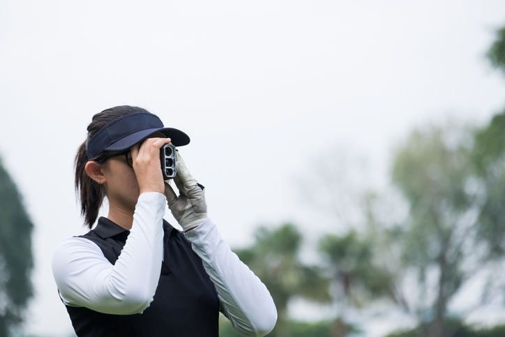 An Asian female golfer using a scope range to check the distance to the green